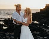 Un couple de mariés sur la plage, en tenue estivale, se souriant amoureusement.