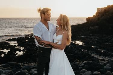 Un couple de mariés sur la plage, en tenue estivale, se souriant amoureusement.